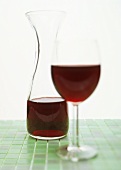 Filled red wine glass with carafe on green tiles