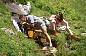 Young couple in mountains, man drinking water from a stream
