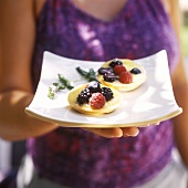 Woman holding two vanilla tartlets with berries