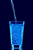 Blaues Wasser wird ins Wasserglas eingeschenkt