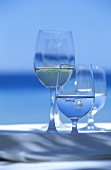 Wasser und Weißwein in Gläsern, Meer im Hintergrund