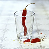 A dried red chili pepper in glass and one lying in front