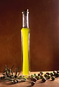 Olivenöl in einer langen, schlanken Glasflasche mit Oliven