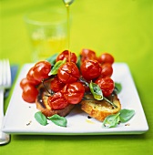 Olivenöl wird über gebackene Tomaten auf Grillbrot geträufelt