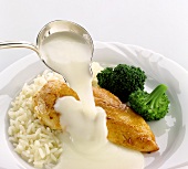 Pouring coconut sauce over fried chicken breast fillet
