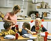 Mother pouring drinks for children sitting at table