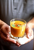 Hände halten Glas mit Möhren-Orangen-Suppe