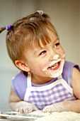 Small laughing girl baking with flour on her face