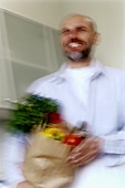 Mann trägt Einkaufstüte mit Gemüse in die Küche