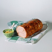 Cold roast pork roll on kitchen cloth with bowl of mustard