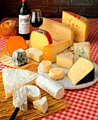Various cheeses, loaf of bread, bottle and glass of red wine