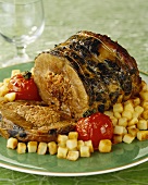 Stuffed roast lamb on diced potatoes with grilled tomatoes