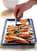 Hand sprinkling herbs over glazed carrots with pine nuts