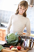 Junge Frau mit Gemüse und Kochtopf in der Küche