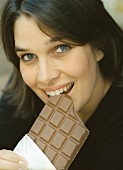 Young woman biting into bar of chocolate (grainy effect)