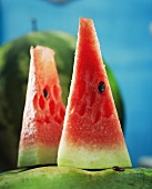 Two pieces of watermelon in front of whole melon