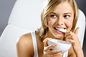 Young woman with bowl of yoghurt, licking her finger