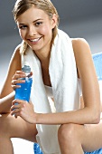 Young woman with towel round neck, sports drink in her hand