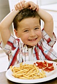 Kleiner Junge vor Teller mit Pommes Frites sitzend