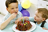 Two boys eating Smarties from birthday cake