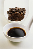 Espresso syrup on ladle in front of ground coffee & beans