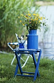 Flowers in a blue milk can on a stool