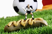 Miniature footballer marking a sausage on football pitch
