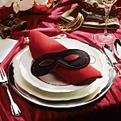 Festive table setting with red napkin & black mask