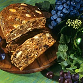 Fruit loaf on wooden plate and red and black grapes