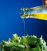 Öl wird aus Flasche auf Salatblatt gegossen