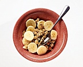 Muesli with fresh banana slices in red bowl with spoon