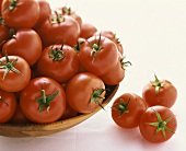 Lots of tomatoes in a bowl and three tomato beside it