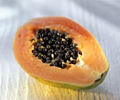 Half a papaya with seeds on a light background
