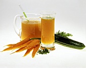 Carrot juice in glass and jug; carrots, cucumber, herbs