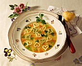Herzchen-Suppe mit Gemüse auf Teller, daneben Herzbrötchen