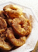 Deep-fried apple rings with cinnamon sugar on white plate
