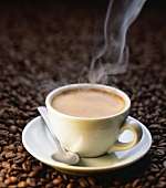 A steaming cup of coffee on coffee beans