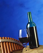 Red wine glass and bottle in sand; pan pipes