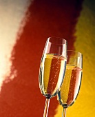 Two champagne against a red and orange painted backdrop