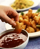 Hand dipping deep-fried shrimp into chili sauce