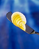 Butter curl on a butter knife against a blue background