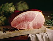 Ham on an old wooden chopping board with juniper berries