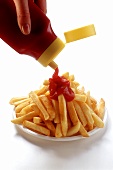 Pouring ketchup on to chips on plate