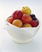 Plums of various colours in white bowl