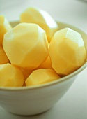 Peeled raw potatoes in white bowl