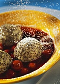 Icing sugar falling on poppyseed dumplings with cherry sauce