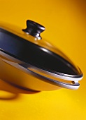 Wok with glass lid on yellow background