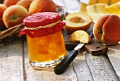 Peach preserve in jam jar in front of fresh peaches