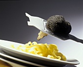 Ribbon noodles on a plate, above a black truffle on a plane
