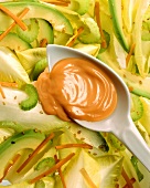 Cocktail salad dressing on spoon above avocado & chicory salad